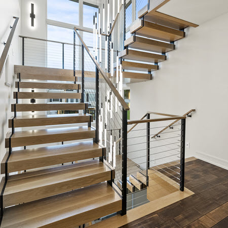 Double Stringer floating stair ascends three stories in a residential home. The stairs have wood treads and hanrails and there is a large chandelier.