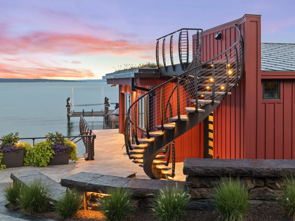 Curved exterior stair leading from the ground to the rooftop of a beach house, featuring curved cable railings and brown stone steps