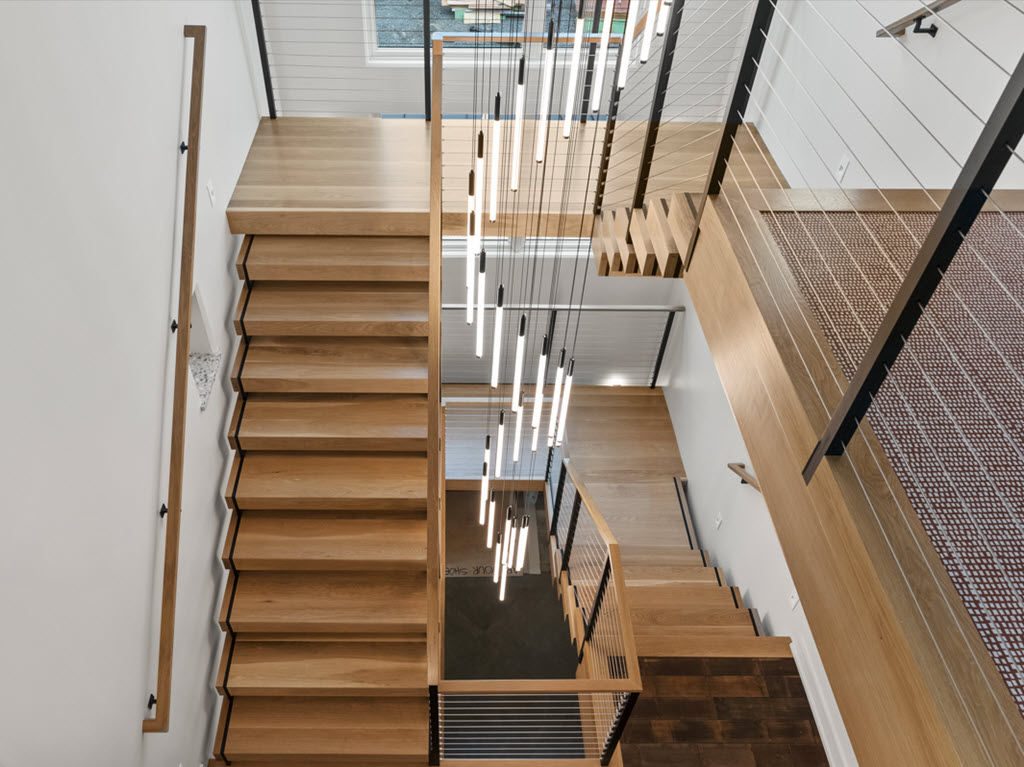 U shaped staircase with double zig zag stringers that slice through the wood treads featuring a cable railing system and LED lighting.