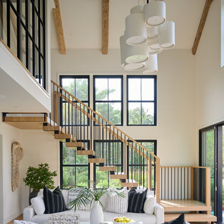 Double stringer floating staircase with spindle railings and white oak treads and handrails in a contemporary setting. The expansive windows allow for natural light to flow throughout the room with white couches.