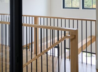 Metal spindle railing wraps a stairwell with white oak handrails