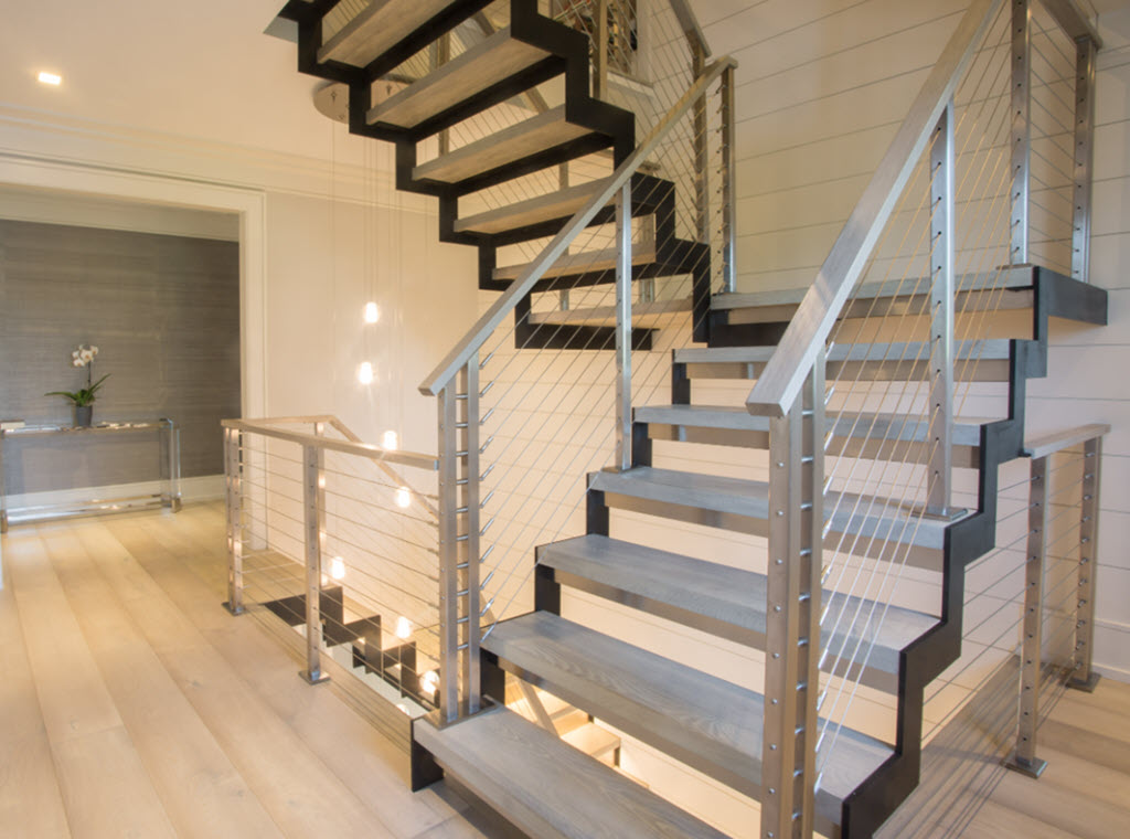 Stainless steel cable railings on a zig zag steel stringer in a second level hall that leads to the bedroom. The floors are white oak and match the wood treads.