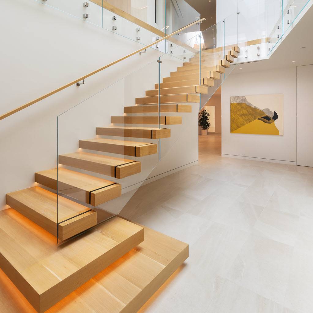 Cantilevered staircase with glass railings gracefully flows down the stairs. Led lighting on each tread adds ambiance to the entry of a modern home.