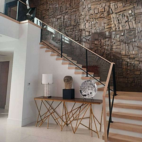 Black metal posts frame the glass on a staircase and balsony. The wood treads match the wood top rail that waterfalls down the tront of the handrail. The staircase perfectly complements the rustic wood wall design.